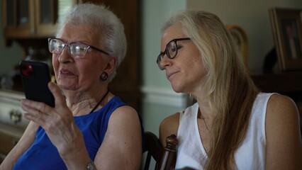 Senior woman and her mature daughter share moments as they look at pictures and connect with others through video calls at home