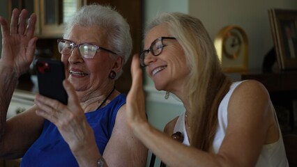 Two women share laughter as they look at pictures and make video calls on a smartphone in their living room