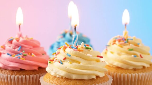 Assortment of delicious vanilla and pink frosted cupcakes topped with colorful sprinkles and flickering birthday candles ready for celebration festivities