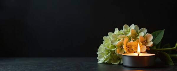 Funeral flower and burning candle on dark background with copy space for message. Symbol of remembrance loss and sympathy for grief and sorrow.