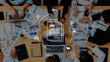 A diverse team engages in a collaborative session surrounded by digital devices and printed reports to analyze data and create effective strategies. Raster