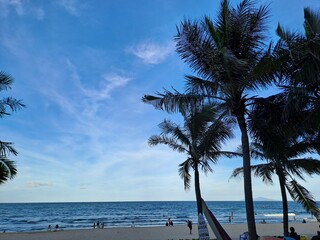 Beautiful coastline landscape featuring tall coconut palms and people relaxing on the sand near the blue ocean waves