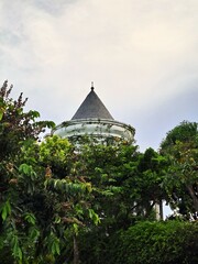 Architectural detail of a classical style building spire surrounded by lush tropical forest foliage under an overcast sky