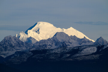Mount Baker stands white against surrounding peaks in shadows in Washington State
