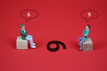 Two miniature figures sitting on a wooden block against an red background, engaged in conversation,...