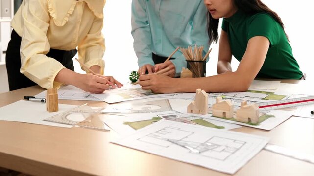 Smart architect and safety engineer discussion about building blueprint on table with architectural document, measurement tools and wooden block scatter around at modern office. Closeup. Delineation.