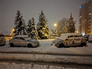 Winter night in the city with snow-covered cars, sidewalks and roads. Snow disaster in a housing estate in Eastern Europe.
