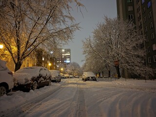 Winter night in the city with snow-covered cars, sidewalks and roads. Snow disaster in a housing estate in Eastern Europe.