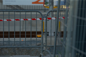 wide view temporary barrier with tape across work zone, inspector surveying perimeter and concrete slabs, empty equipment and muted daylight convey paused construction activity
