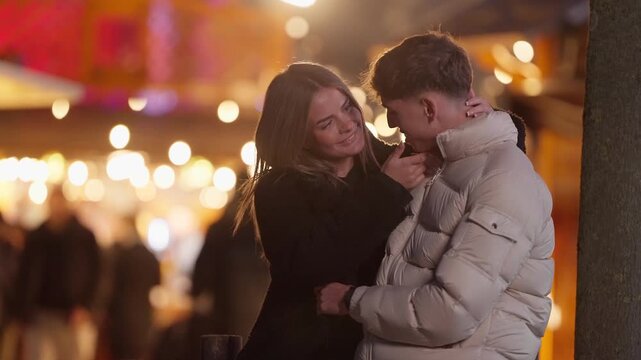 A romantic couple embraces in Paris France at night The woman hugs the man affectionately amidst bokeh lights and a festive outdoor market scene The couple is dressed in winter clothing enjoying a mom
