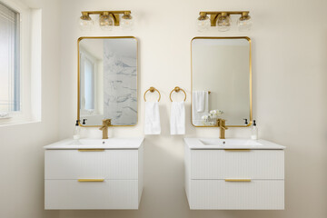 A bathroom detail with floating white fluted cabinets, gold faucets on white sinks, and gold lights...