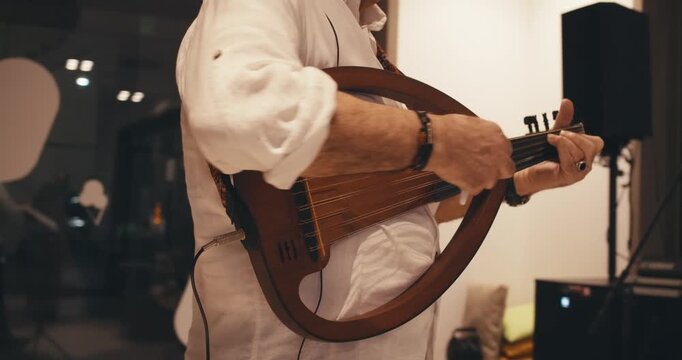 man plays unusual original traditional authentic stringed instrument balalaika ukulele guitar. close-up view man hand playing strings. musical stringed wooden instrument close up. musical performance