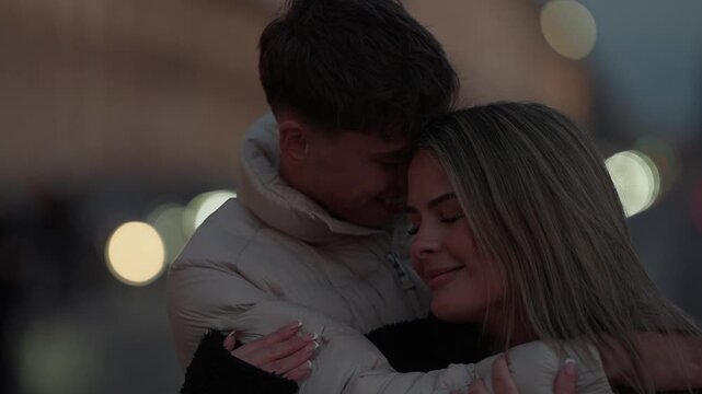 A young couple embraces in Paris France at dusk The man and woman are hugging outdoors with soft bokeh lights in the background sharing an intimate moment of romance and affection.