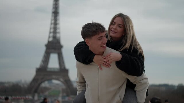 A romantic couple enjoys a piggyback ride in Paris France with the Eiffel Tower in the background The young woman embraces the man showcasing their love and affection. This clip captures a travel vaca