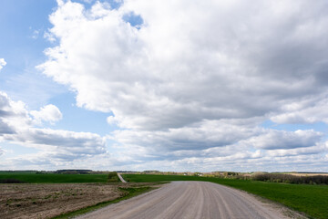 Blue sky with cumulus clouds over a gravel road in the middle of a field