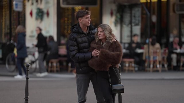 A romantic couple embraces on a Parisian street The background features blurred cafes and pedestrians creating a classic Parisian scene The shot captures a moment of love and affection in the heart of