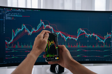 Investor person holding smartphone displaying real-time cryptocurrency or stock market charts, observing fluctuations and making informed decisions for online trading on larger screen, close-up.