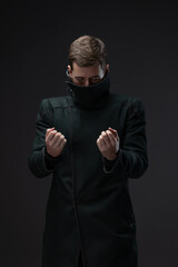 Melancholic cyberpunk style: man in oversized collar coat posing on studio gray.