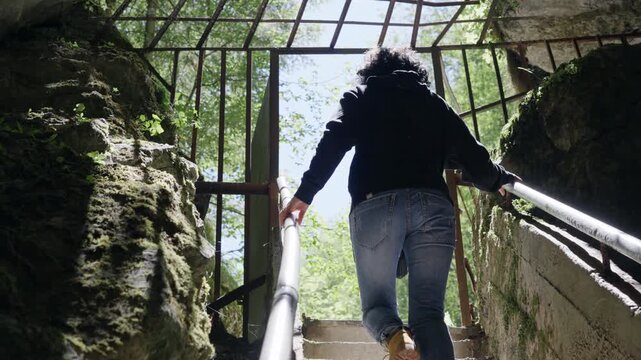 Woman climb on stairs visiting mystic view underground cave Devil's Throat (Dyavolsko garlo ) cave in the Rhodope Mountains, abundantly overgrown with deciduous and evergreen forest 