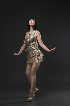 Flapper era femme fatale in short gold dress, Art Deco jewelry and bob. Dancing