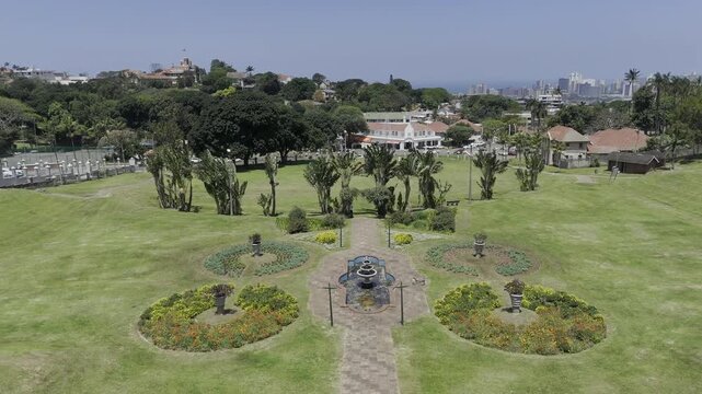 Drone flies south, low over Jameson Park, then over neighborhood to reveal view of coast on sunny day in Windermere neighborhood in Durban, South Africa
