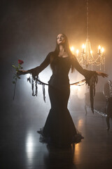 A gothic femme fatale with long straight hair and dark makeup wears a black godet skirt dress with corset, posed in a luxurious dimly lit gothic interior.