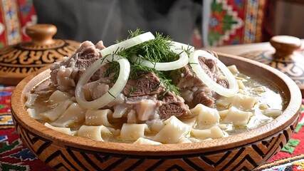A closeup view of a traditional Central Asian Beshbarmak dish featuring tender boiled meat wide flat noodles and garnished with fresh onion rings and dill served in an ornate wooden bowl on a colorfu.