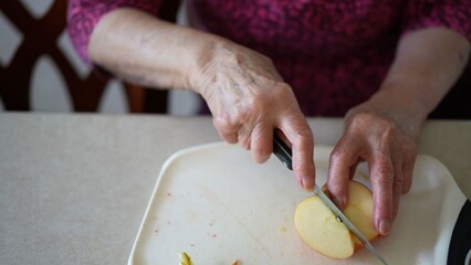 Senior woman slices apples for a fruit salad while talking to family on a video call in her kitchen during the morning