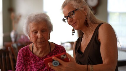 An elderly woman and her mature daughter look at photos and make video calls while enjoying their time together at home