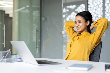 Young professional woman smiling and relaxing at her desk, feeling satisfied and successful after completing work or during a break from her project in a modern office