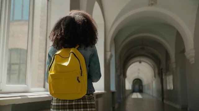 Back view African female student walking go alone in empty university corridor American girl schoolgirl woman with schoolbag lady hallway college high school hall walk move going class education study