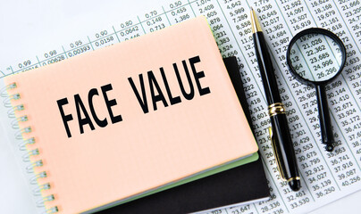 FACE VALUE - words on a yellow notebook on a background of digital tables, a magnifying glass and a...