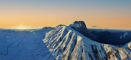 Majestic snow-covered mountain peaks at sunset with golden sky and deep shadows in a panoramic winter landscape.