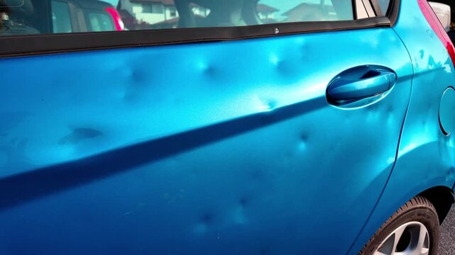 Car doors visibly damaged by hail, with dents on the metal surface in natural light.