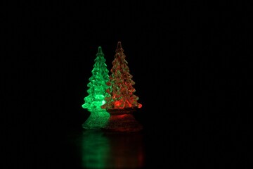 Miniature Christmas trees. Red and green all lit up in the darkness with reflections on the surface of the desk.