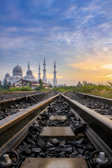 Obraz premium Architectural Grandeur of Mosque Towers Over Intersecting Railway Tracks at sunrise