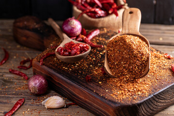 Chili powder in a wooden bowl and with a wooden spoon, along with garlic, shallots, and a mix of Asian spices, are arranged on a wooden table, conveying the concept of spicy food.