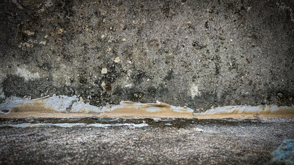 Grunge texture of a concrete wall with paint smudges, mold stains, and part of a concrete floor in horizontal orientation,