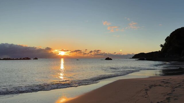 Peaceful morning at the beach with glowing sun on the horizon and gentle waves