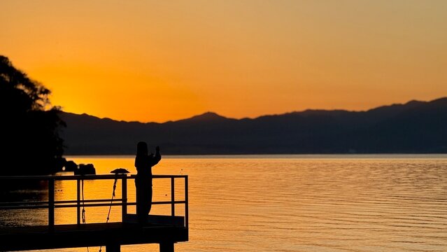 A silhouette of a person standing by the calm Lake Biwa at sunset