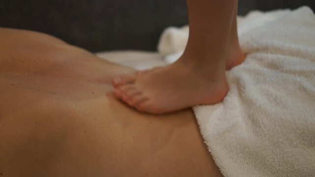 A young child carefully walks on his mother's back to provide a traditional barefoot massage (ashiatsu) at home or in a wellness setting.