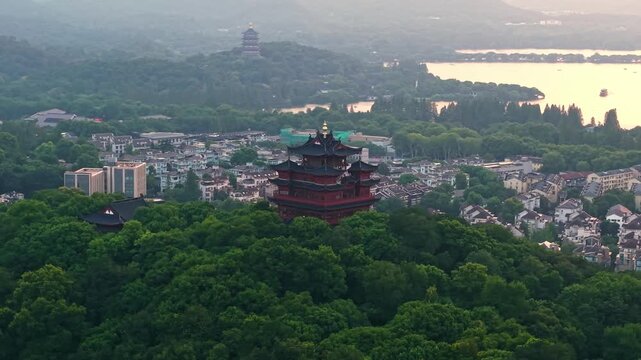 Aerial view of Chenghuang pagoda at sunset over Xihu lake in Hangzhou featuring mountains and lush green trees