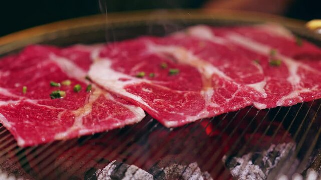 Grilling thin slices of Beef on a charcoal barbecue in an indoor restaurant during the evening
