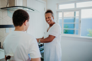 Fototapeta premium Happy African American mother smiling at her son who is hiding flowers behind his back in a bright kitchen, a heartwarming family surprise moment.