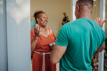 Happy senior African American woman greeting a visitor with a gift at her front door during the Christmas holiday season. © Nexa