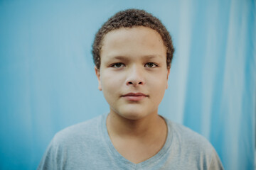 Portrait of a calm young mixed-race boy with curly hair looking at the camera against a blue background.