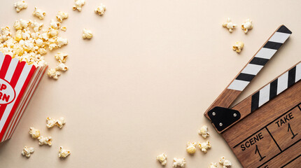 A mouthwatering still life scene featuring popcorn overflowing from a classic striped container, alongside a wooden clapperboard, perfectly captures the allure of a movie night.