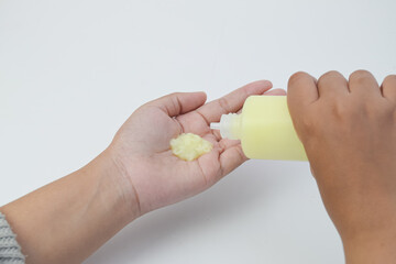 Yellow lotion in plastic bottle and texture detail of cosmetic product on hand over white background.