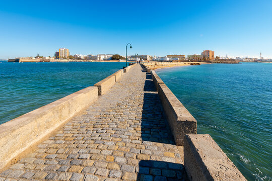 View of the sandy beaches and seaside city from the historic stone bridge walkway, Paseo Fernando Qui&ntilde;ones, that connects La Caleta beach to the Castle of San Sebastian, in Cadiz, Spain.