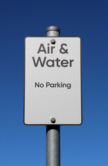 Air & Water and No Parking sign attached to a metal pole against a clear blue sky background